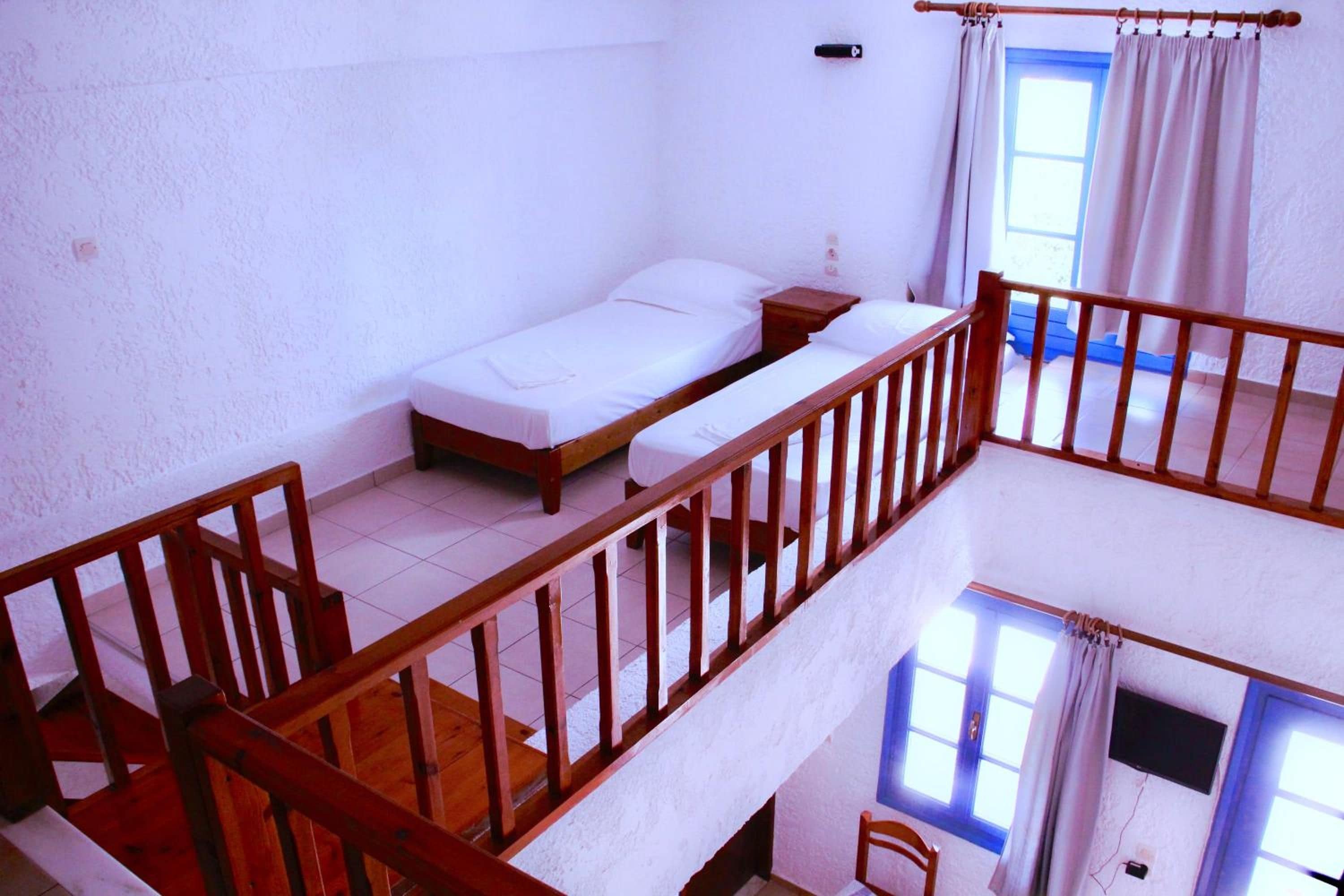 Habitación tipo dormitorio con una cama individual, baranda de madera y ventana con cortinas.