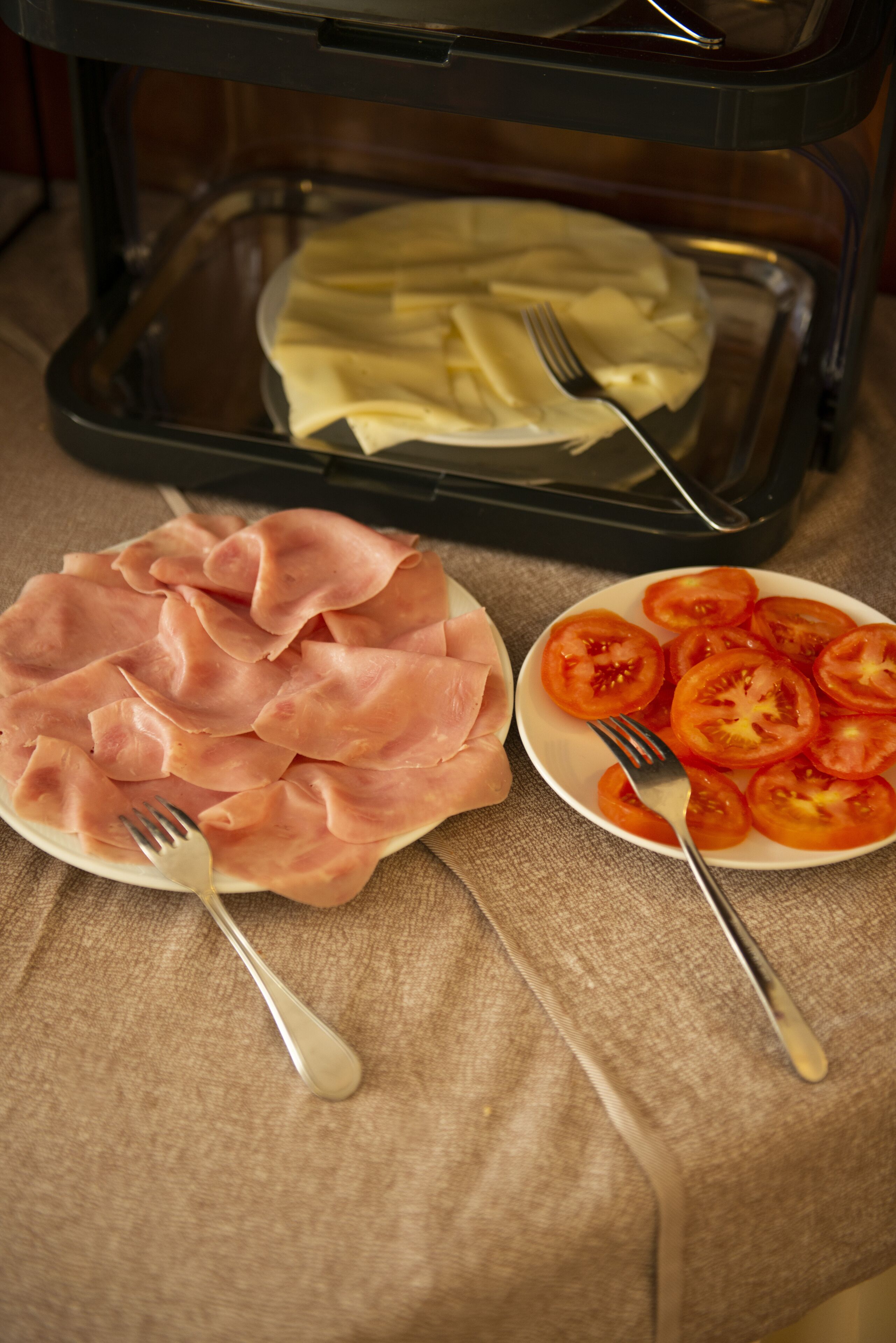 A tray with sliced ham and tomatoes on a table.