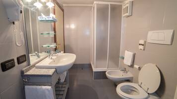 A modern bathroom with a shower, two sinks, a toilet, and a hairdryer.