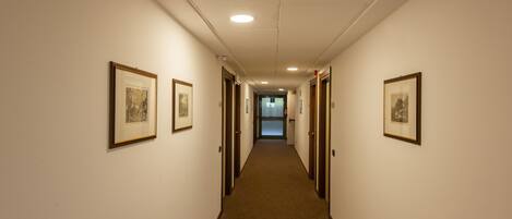 A hotel hallway with framed pictures on the walls, doors leading to rooms, and a carpeted floor.