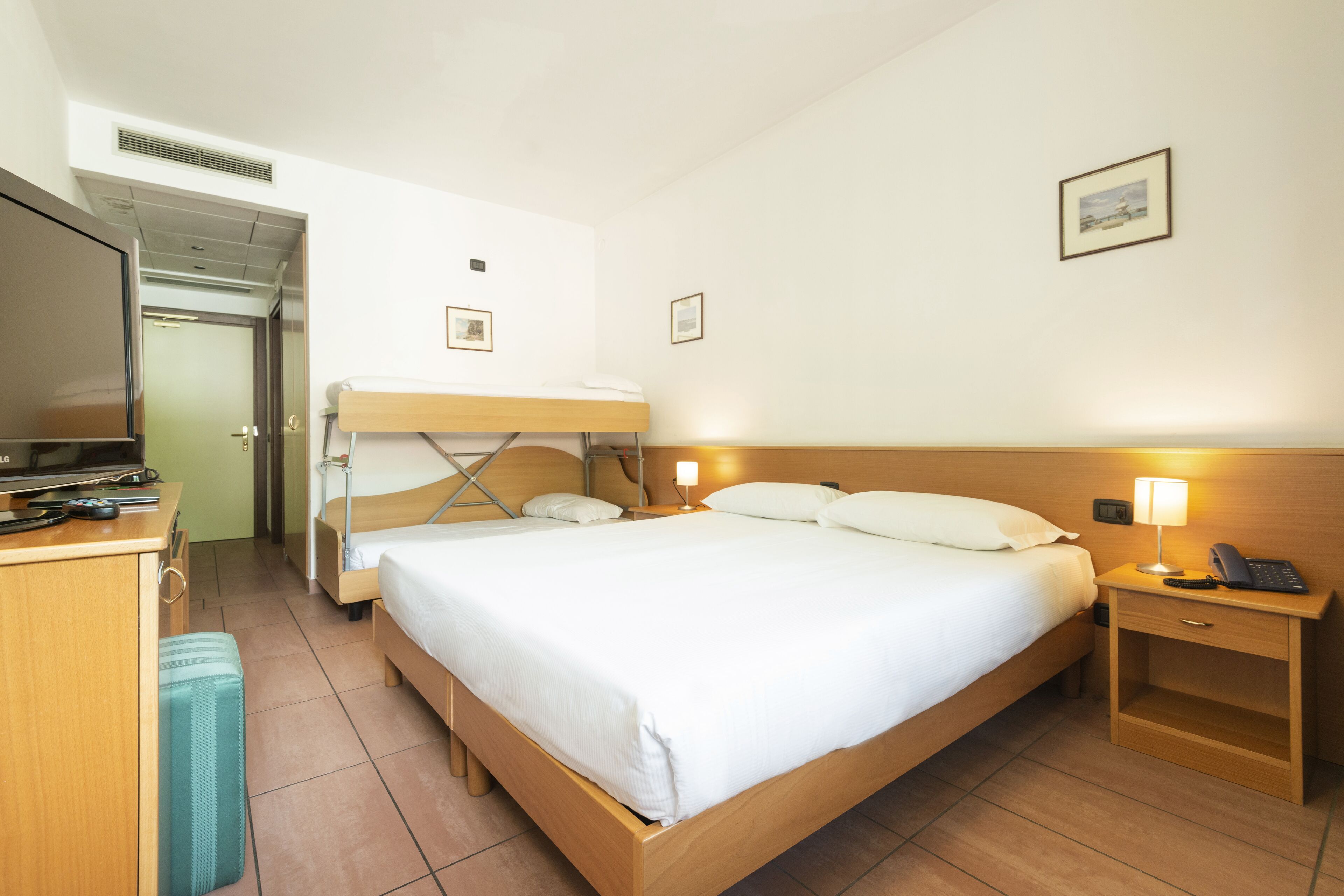 Une chambre d’hôtel avec un lit superposé, un bureau avec un ordinateur portable, une table de chevet avec une lampe et une petite table de chevet avec un téléphone.