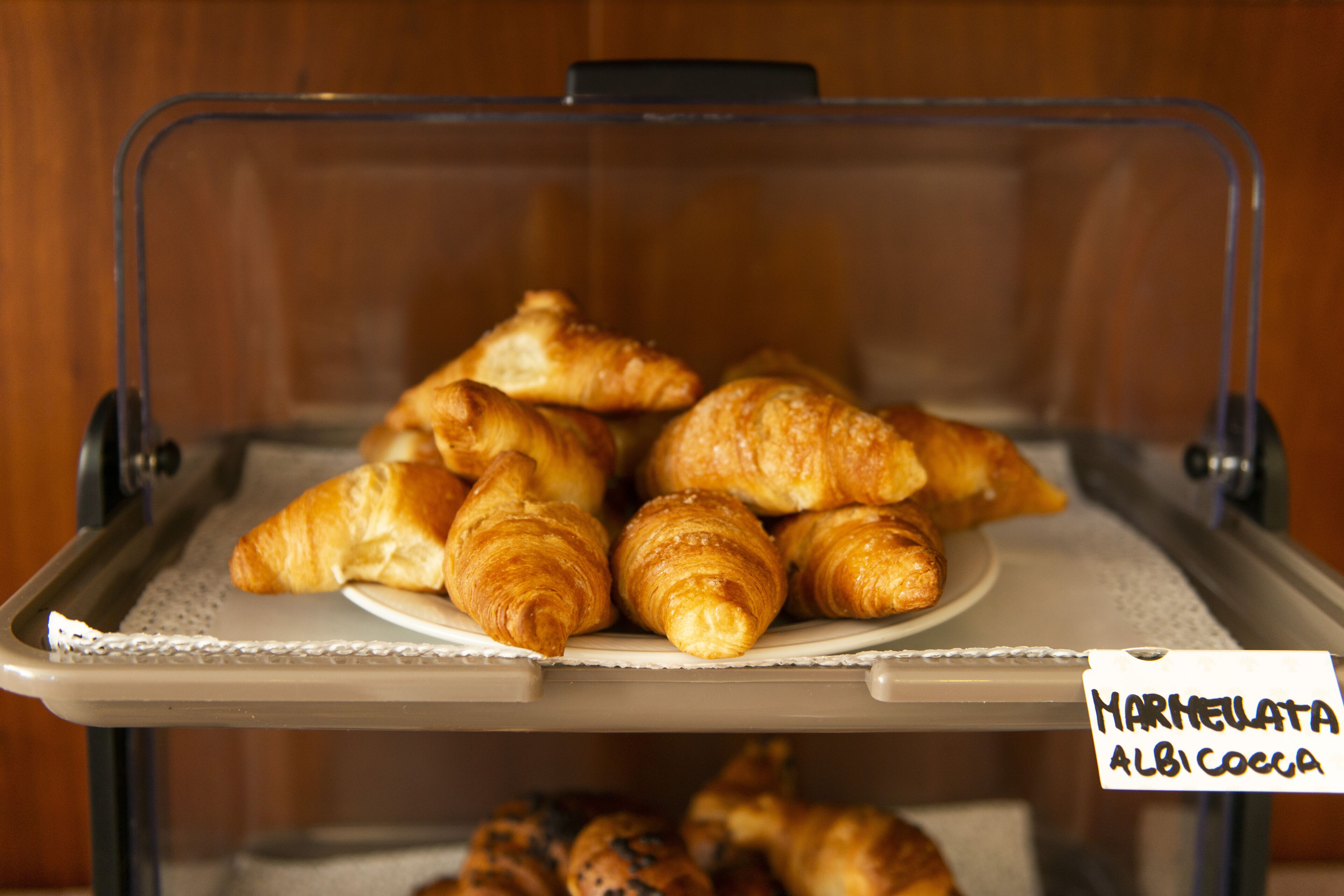 Une vitrine contenant une variété de pâtisseries, notamment des croissants et des muffins, avec une étiquette indiquant : « Marmeleata Albi Coeca ».