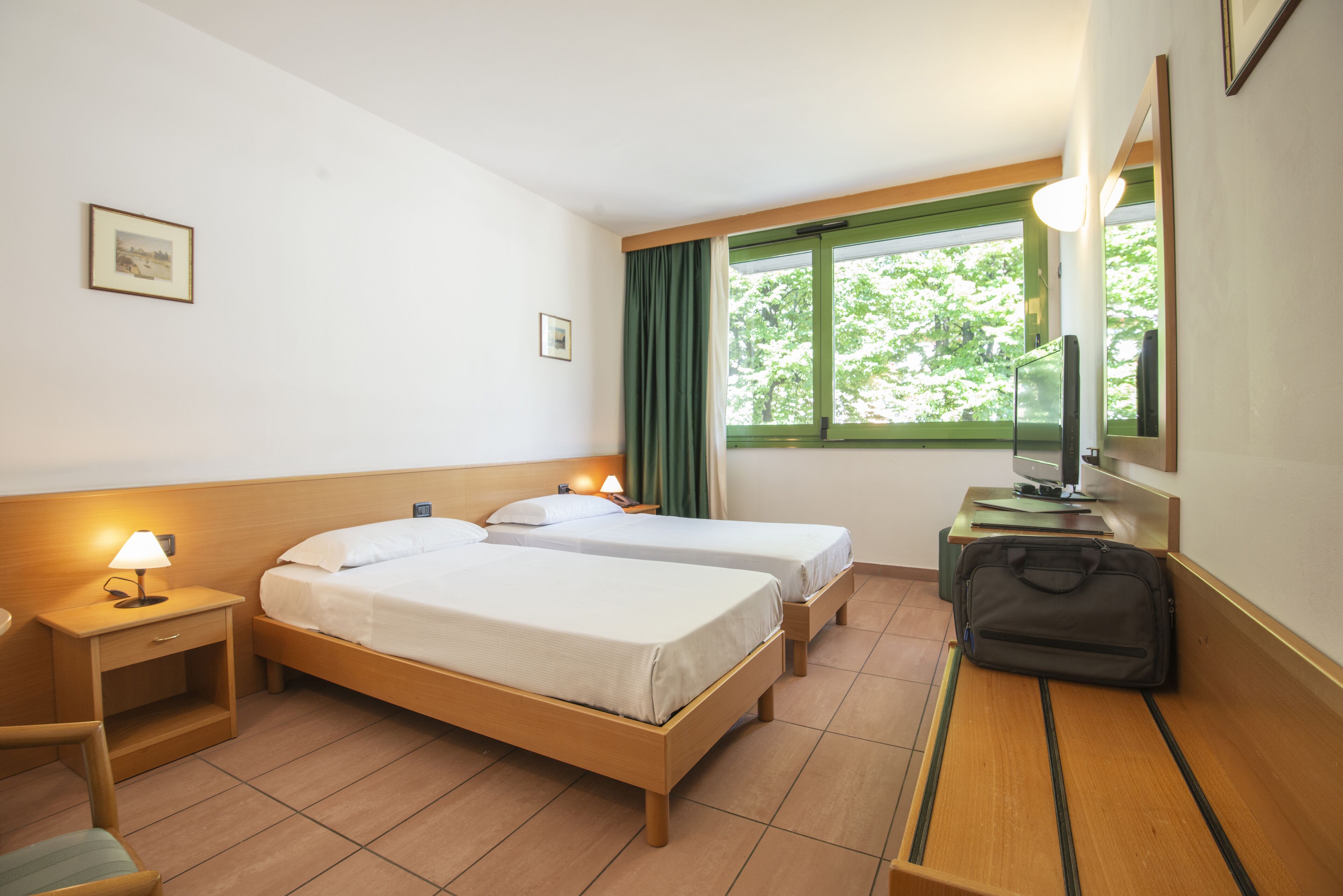 A hotel room with two beds, a desk, a chair, a TV, and a window with curtains.