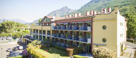 Un hotel de varios pisos con balcones, estacionamiento y montañas al fondo.
