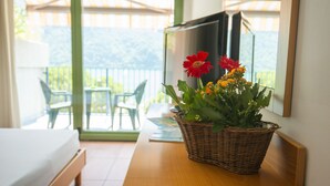 Une chambre avec un lit, un panier en osier rempli de fleurs, une télévision et un balcon avec des chaises et une table.