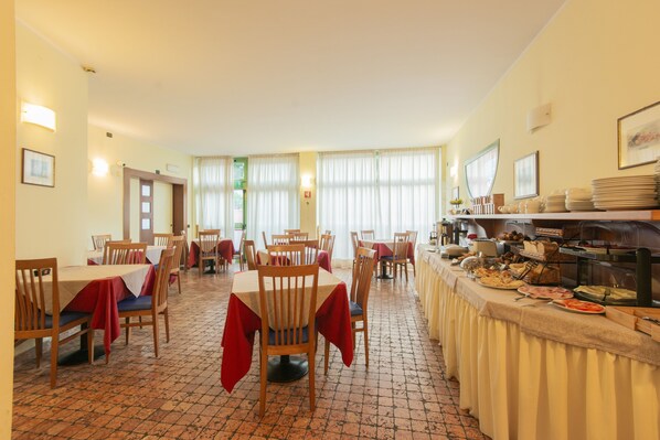 A dining area with multiple tables and chairs, a buffet line with various food items, and a tiled floor.