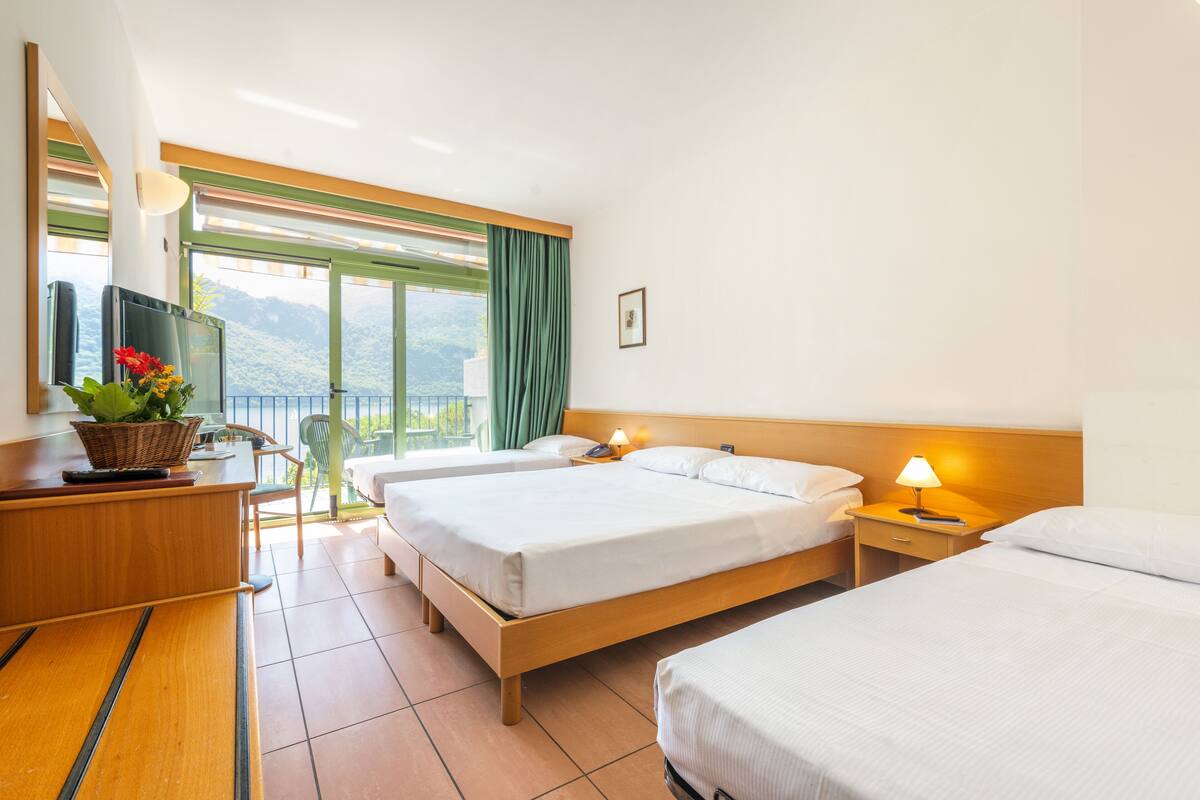 Habitación de hotel con dos camas, un escritorio con computadora y un florero, una silla y vistas al exterior.