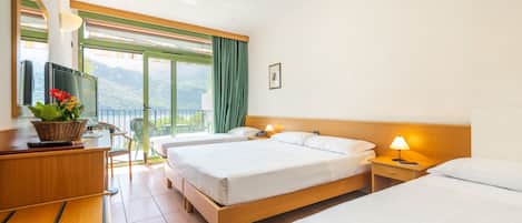 A hotel room with two beds, a desk with a computer and a basket of flowers, a chair, and a view of the outdoors.