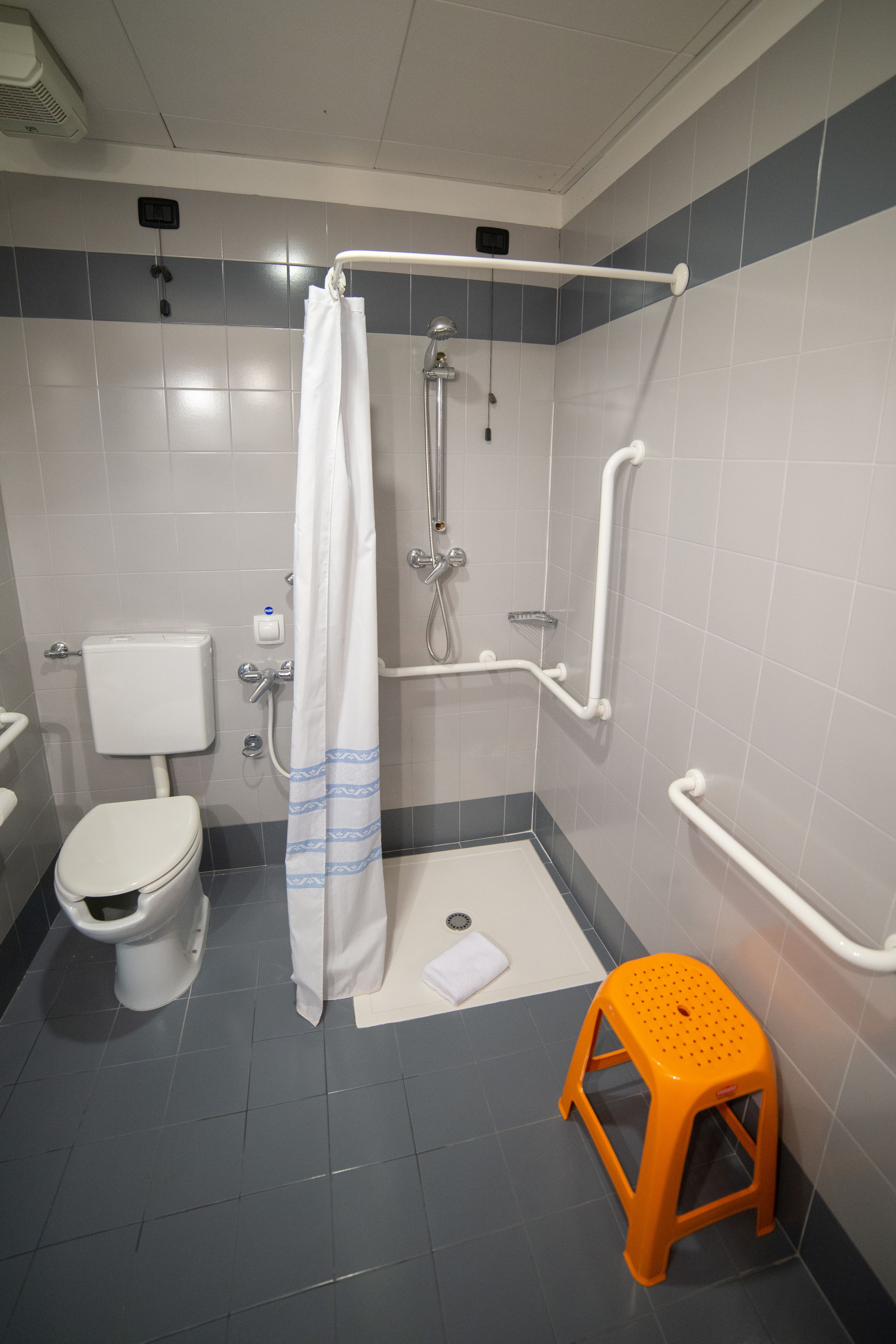 A bathroom with a toilet, shower, grab bars, and a small orange stool.