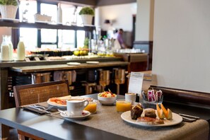 Un desayuno con diversas opciones de comida, como un tazón de fruta, un plato de pasteles y una taza de café.