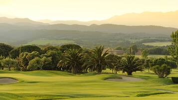 Un campo de golf con colinas ondulantes, palmeras y montañas a lo lejos.