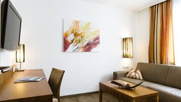 Ein modernes Hotelzimmer mit einem Holztisch, einer Couch, einem Flachbildfernseher und einem Bild an der Wand.