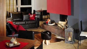 A modern living room with a fireplace, leather sofa, and a dining area. - Hotel Kapeller (Innsbruck)