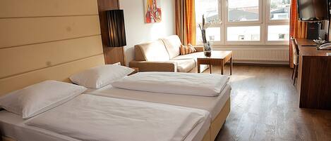 Une chambre d’hôtel avec deux lits, un canapé, une petite table, une télévision et une fenêtre avec des rideaux.
