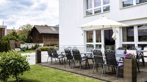 A patio with outdoor seating, a white building, and a wooden play structure in the background. - Hotel Kapeller (Innsbruck)