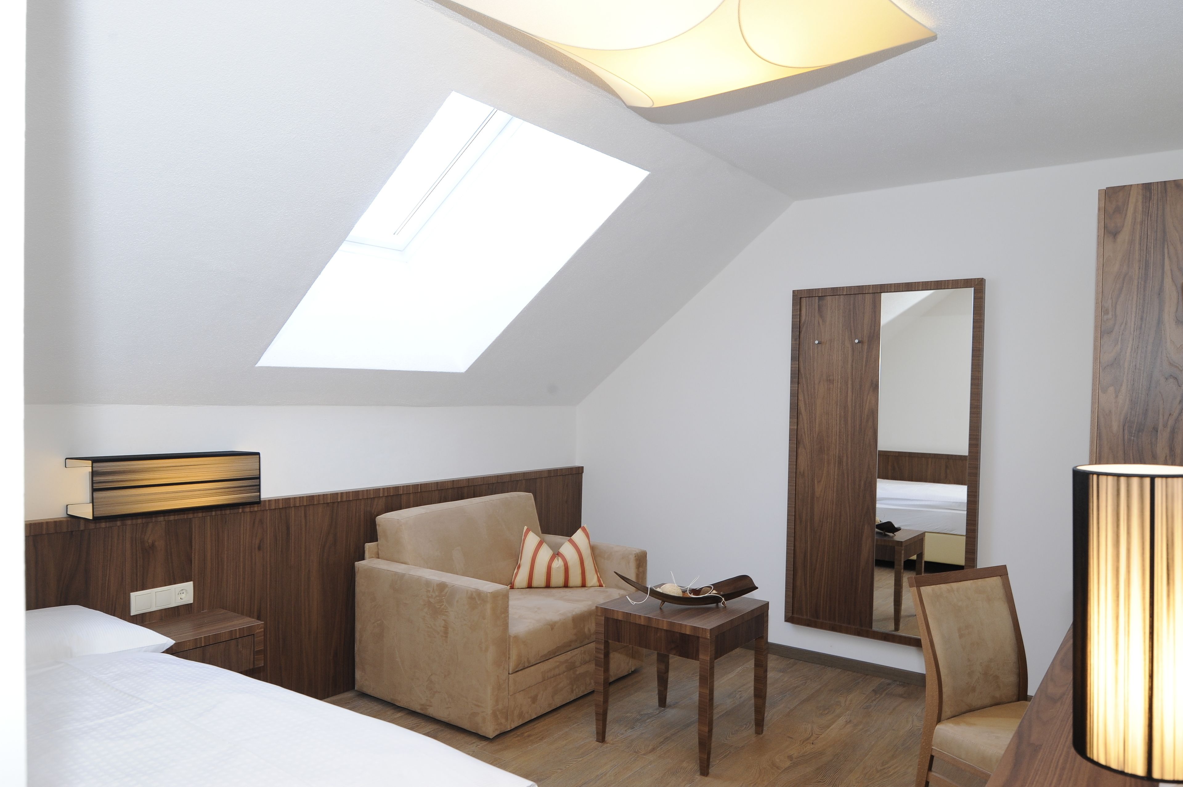 Habitación de hotel con sofá, una mesita, lámpara, espejo y tragaluz.