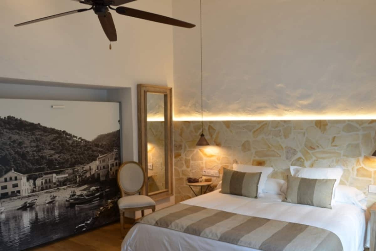Ein Schlafzimmer mit Bett, Deckenventilator, Nachttisch, Lampe, Stuhl und einem an der Wand befestigten Spiegel.