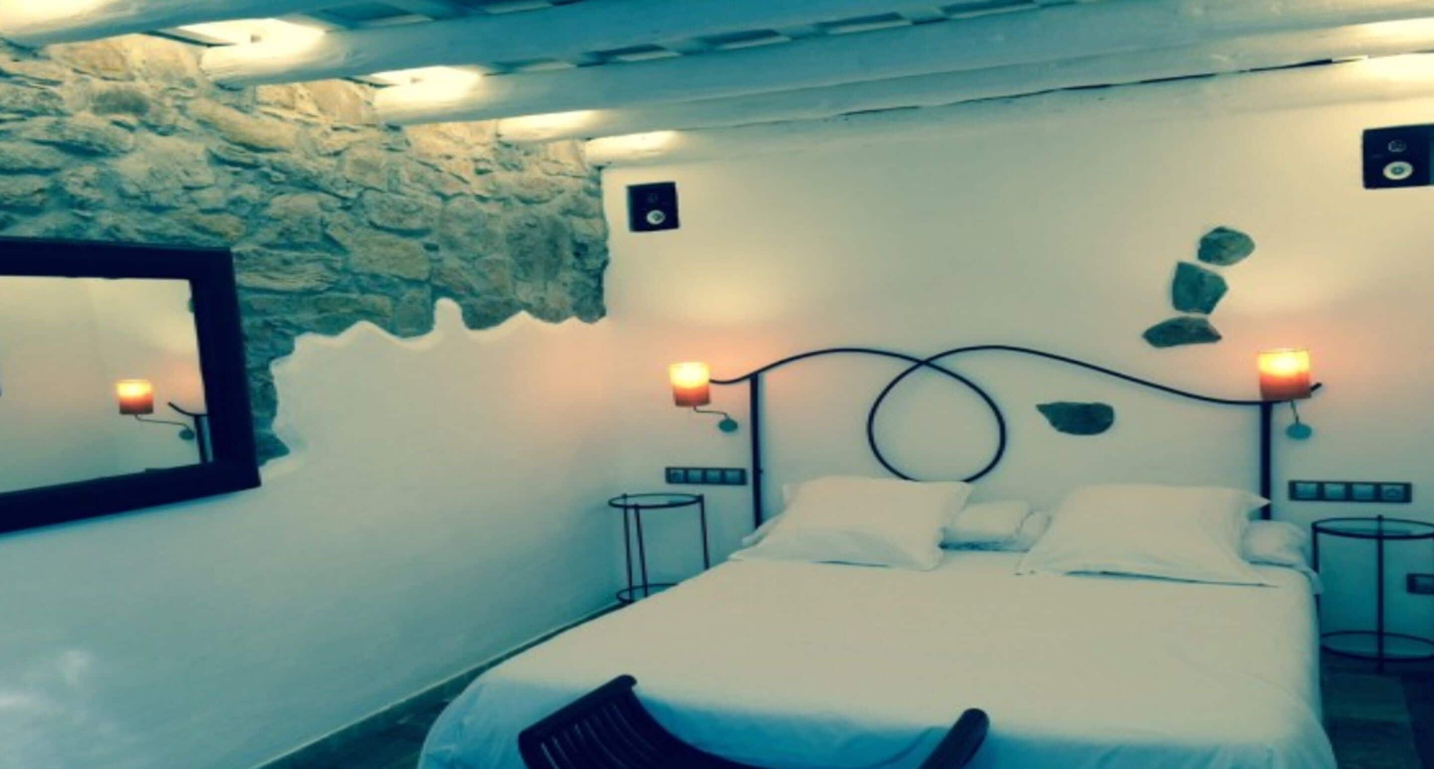 A bedroom with a stone wall, a bed with white bedding, two bedside tables, and wall-mounted lamps.