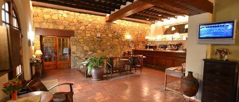 A spacious lobby with a stone wall, wooden ceiling beams, a bar area, and a television mounted on the wall.