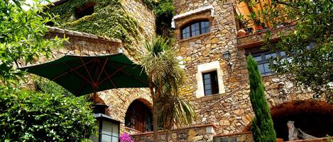 Un edificio de piedra con una sombrilla verde, una palmera y un banco.