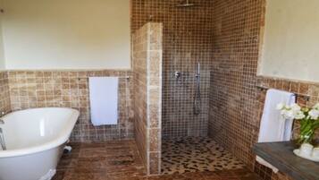 Un baño con una bañera independiente, zona de ducha con paredes de azulejos y suelo de mármol.