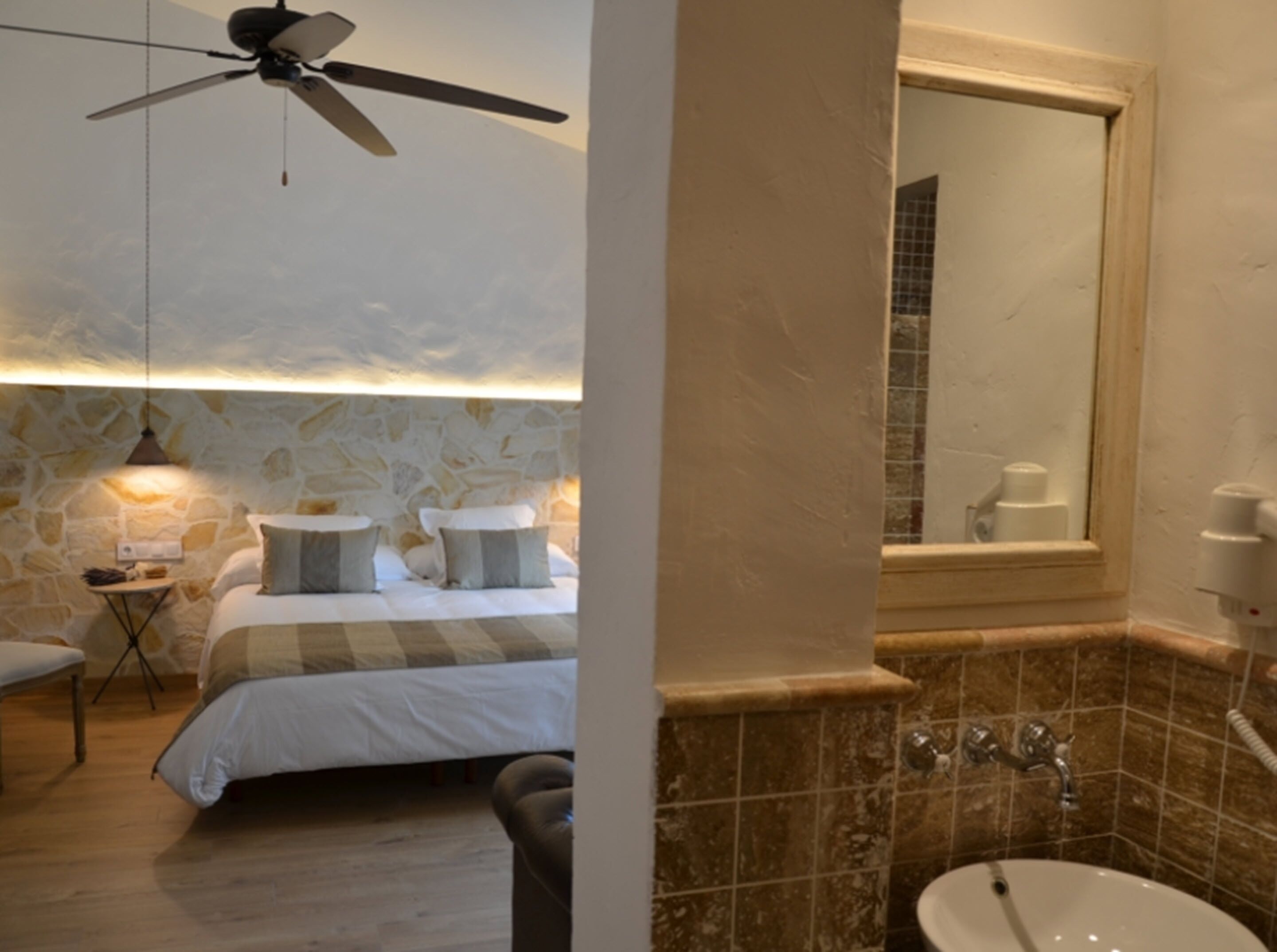 A bedroom with a bed, bedside table, lamp, and a ceiling fan.