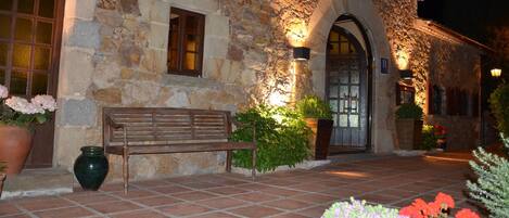 A stone building with a bench, potted plants, and a tiled entrance.