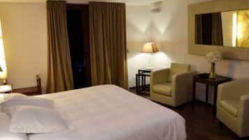 Habitación de hotel con una cama grande, dos sillones, una mesita con una lámpara y un espejo en la pared.