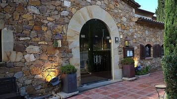 Un edificio de piedra con entrada abovedada, mesas al aire libre y plantas en macetas.