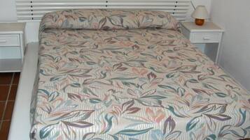 Una cama con una colcha estampada con motivos florales, dos mesitas de noche con lámparas y un suelo de baldosas.