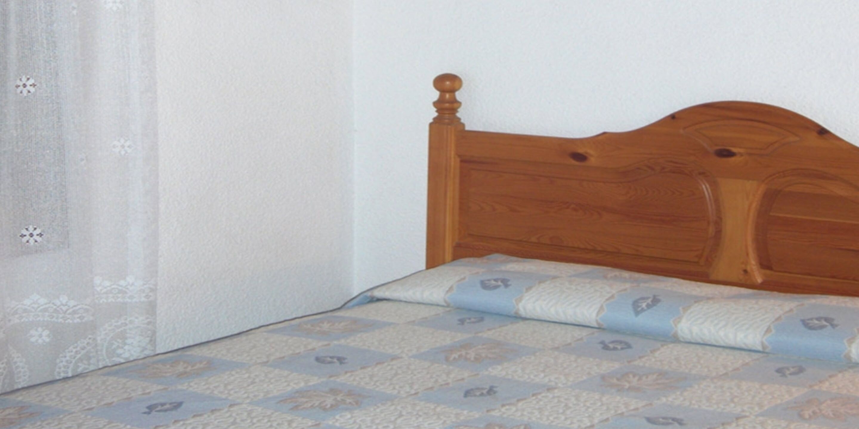 A single bed with a wooden headboard and a patterned bedspread.