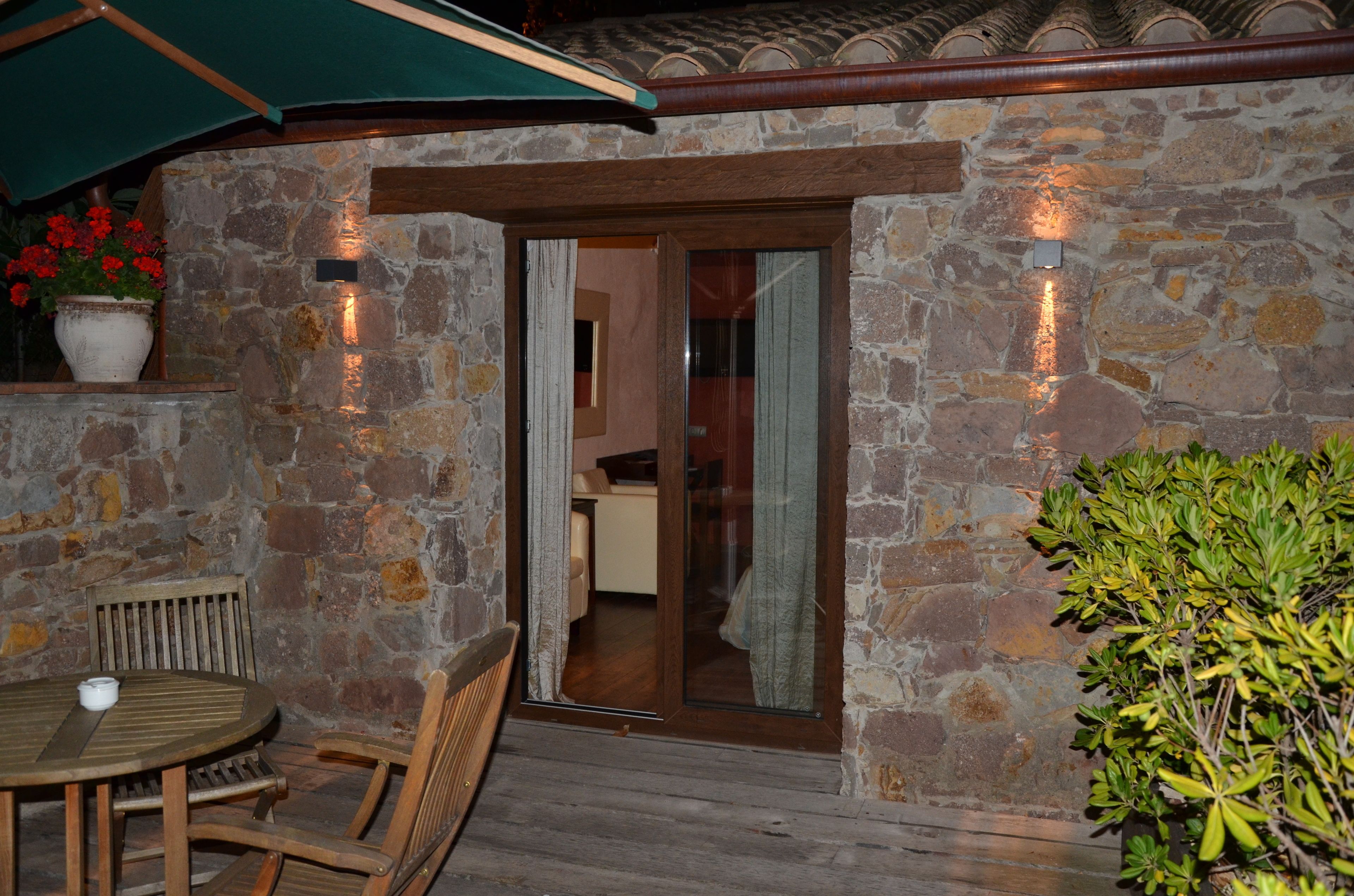 A stone exterior with a wooden deck, a table with chairs, and a potted plant.