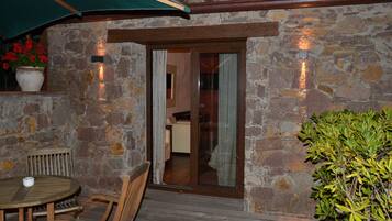 Fachada de piedra con una terraza de madera, una mesa con sillas y una planta en maceta.