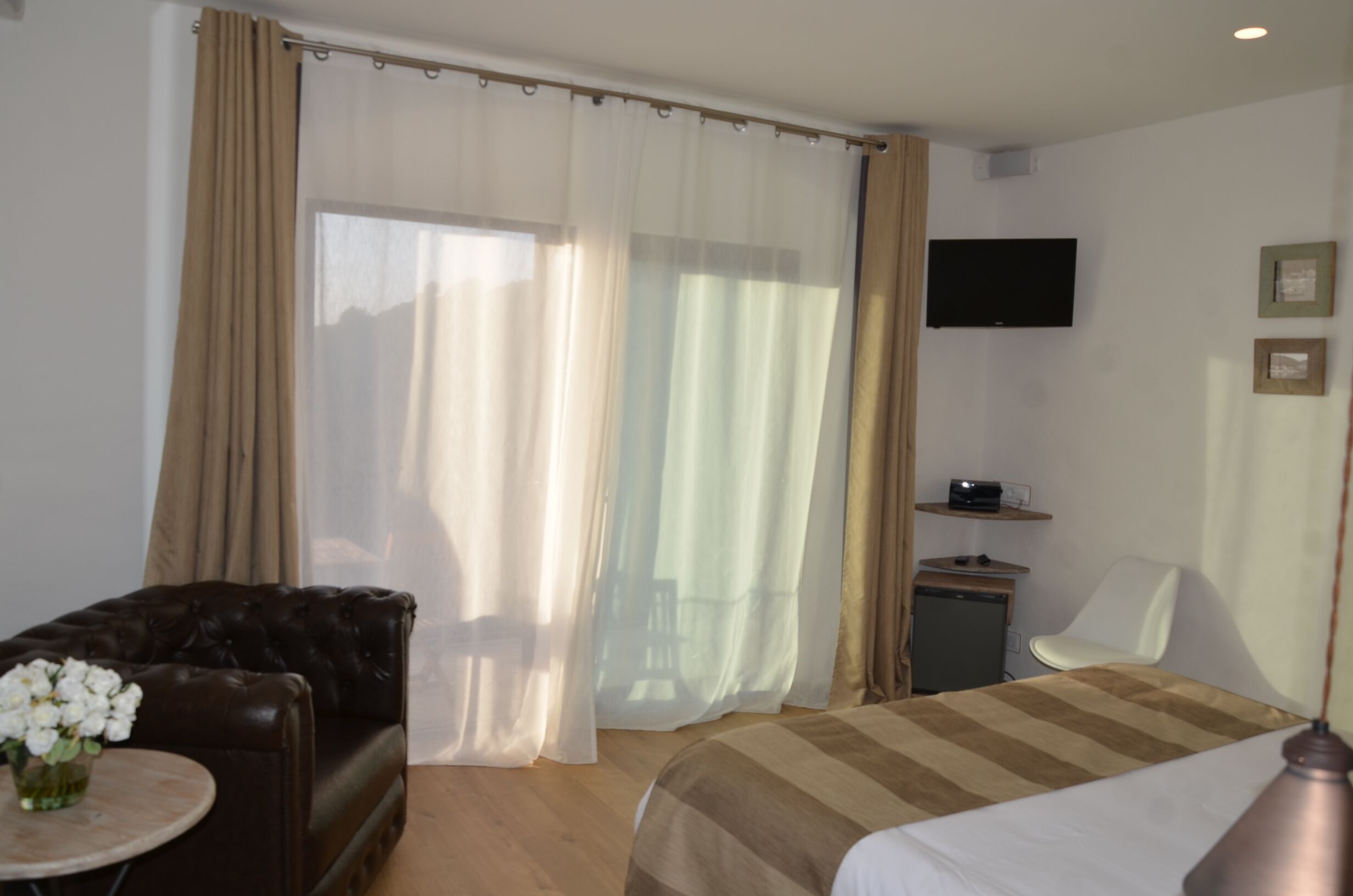 Et hotelværelse med en seng, en sofa, et lille bord med blomster, et fjernsyn, en stol og et skrivebord med en radio.