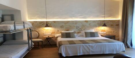 Une chambre avec des lits superposés, un grand lit et un mur en pierre.
