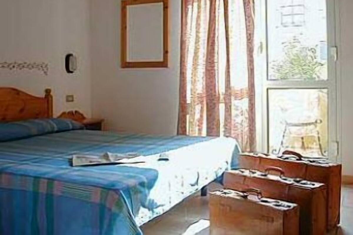 Une chambre à coucher avec un lit, une fenêtre avec des rideaux, un miroir et une tête de lit en bois.