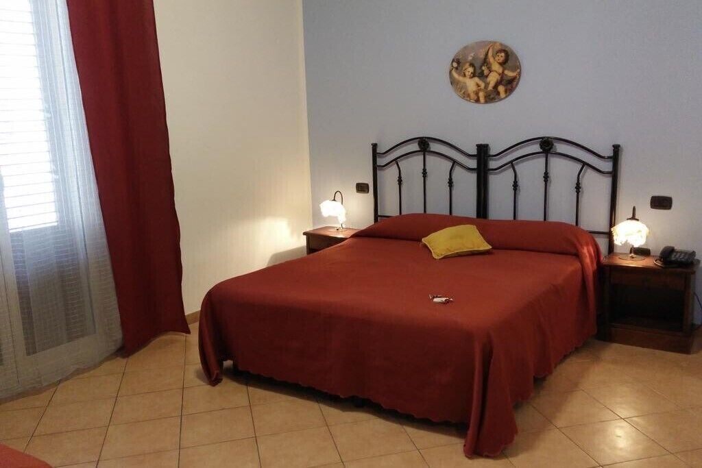 Un dormitorio con una cama grande, dos mesitas de noche con lámparas, una cortina roja y un cuadro en la pared.