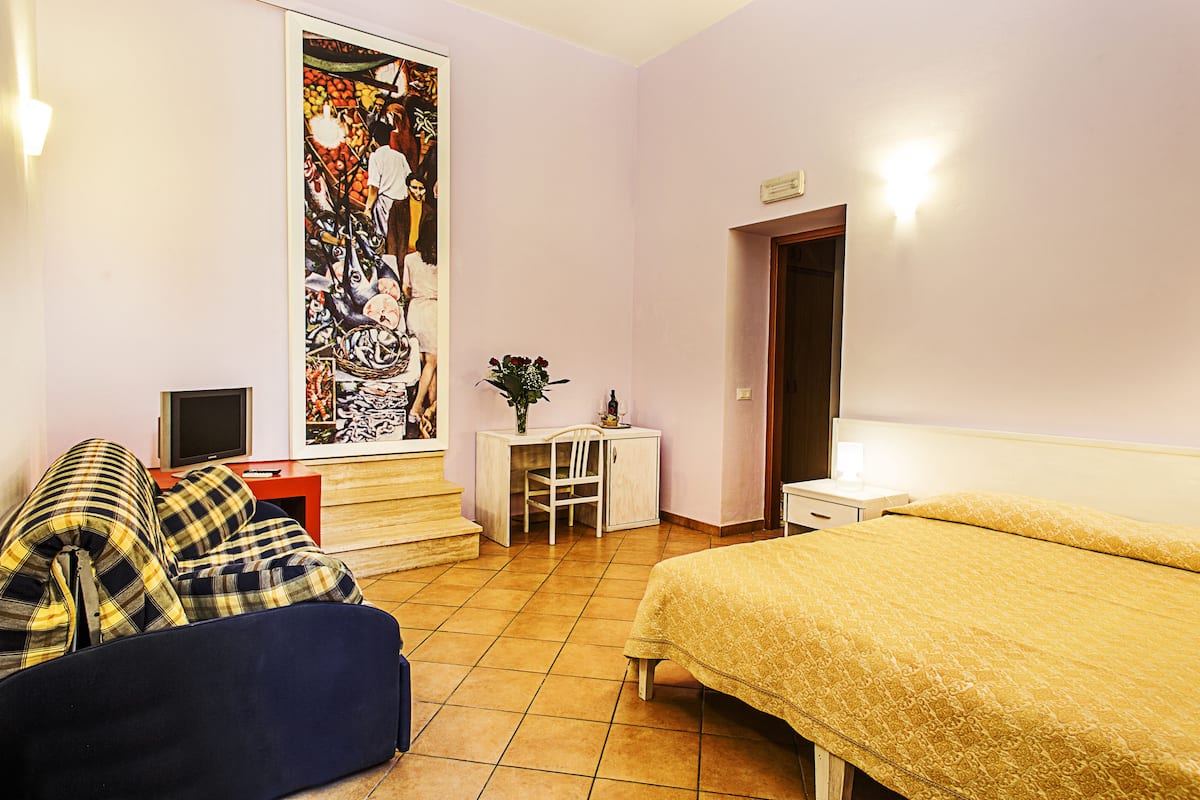 Une chambre à coucher comprenant un lit, un bureau, une chaise, un canapé et un grand tableau abstrait accroché au mur.