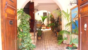 Um pátio com um caminho pavimentado, plantas em vasos, portas de madeira e uma pintura na parede.