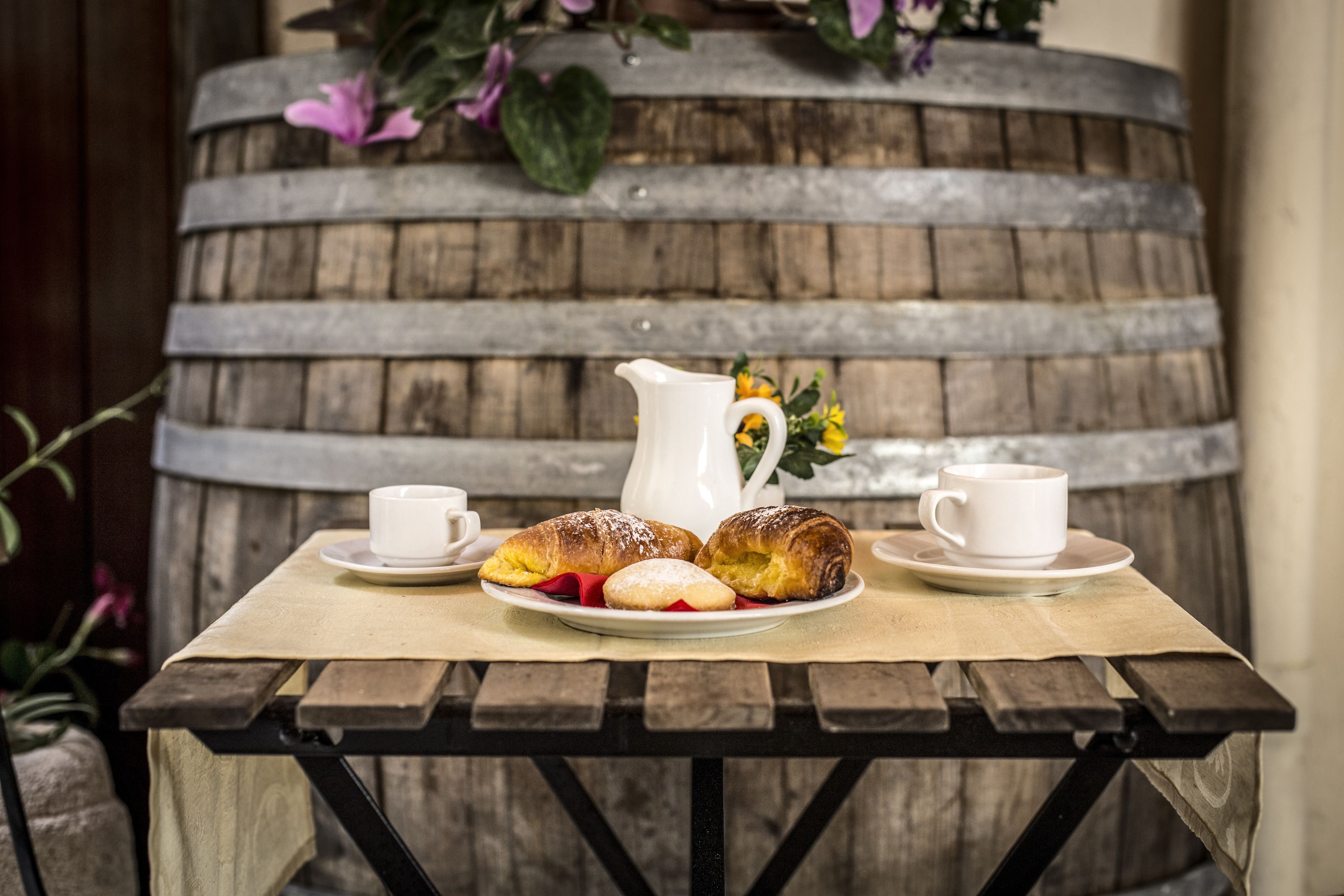 A wooden table with a rustic barrel backdrop, a pitcher, two cups, and pastries.