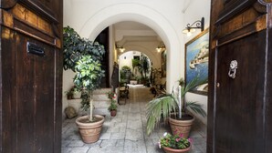 Um corredor com portas de madeira, plantas em vasos e piso de pedra.