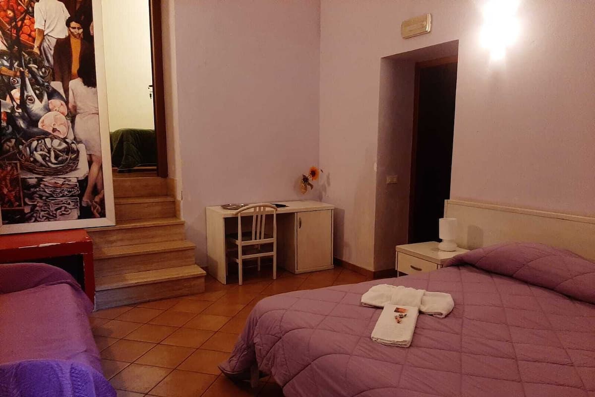 Une chambre d’hôtel avec deux lits, un bureau, une chaise et une petite table sur laquelle est posé un vase de fleurs.