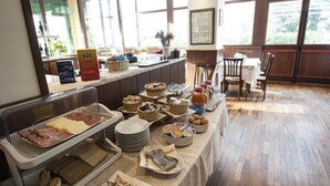 A buffet setup with various food items and utensils on a table, surrounded by windows and a chair.