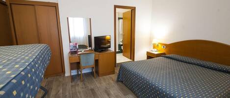 A hotel room with two beds, a desk with a computer, a chair, and a bedside table with a lamp.
