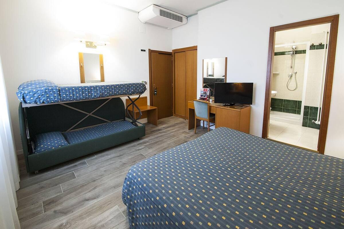 A hotel room with a bunk bed, a desk with a chair, a television, and a shower area.