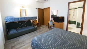 Quarto de hotel com cama beliche, escrivaninha com cadeira, televisão e chuveiro.