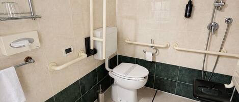 Baño con inodoro, bidé y lavamanos, equipado con barras de apoyo y ducha.