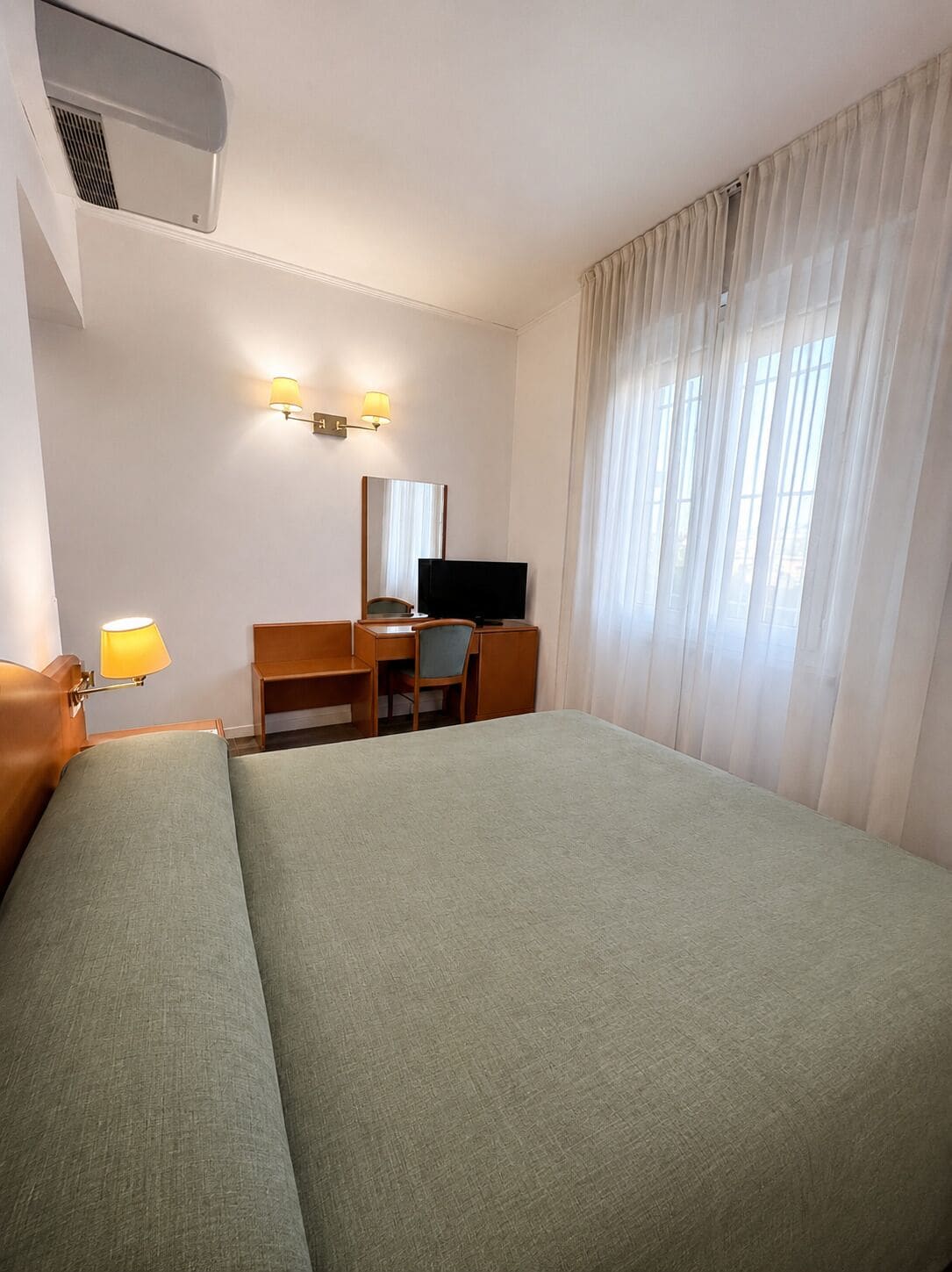 A hotel room with a bed, a desk, a television, and a window with curtains.