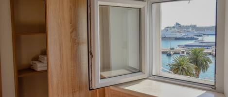 A room with a wooden wardrobe and a window with a view of a cruise ship docked at a marina.