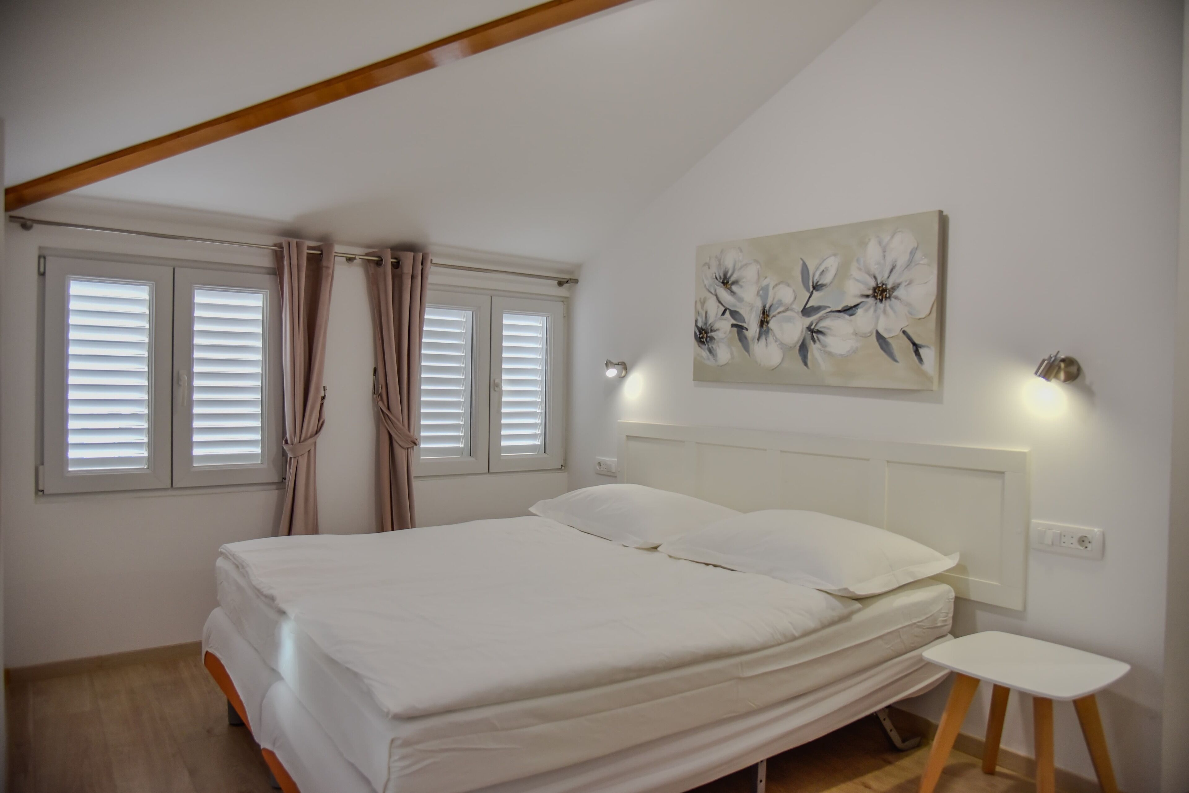 A bedroom with a bed, a nightstand, a painting, and windows with curtains.